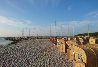Sandstrand med kurvestole, sejlbåde og blå himmel ved Bungalow-kompleks «Gänseblümchen 6» i Tyskland.