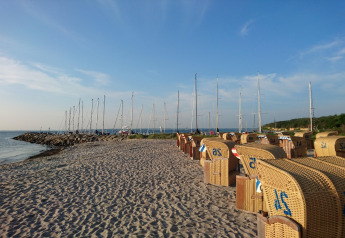 Zandstrand met rieten strandstoelen en zeilboten bij bungalowcomplex «Gänseblümchen 6» in Duitsland.