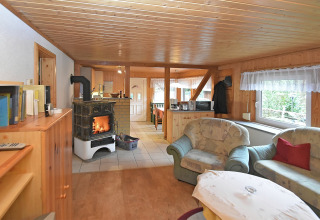 Soggiorno di chalet in Germania con stufa a legna, divani comodi e ampio panorama dalla finestra.