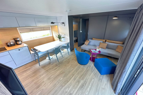 Modern tiny house interior featuring an open kitchen, dining area, living room with blue chairs and sofa.