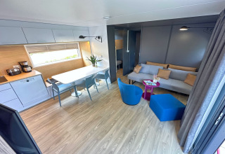 Modern tiny house interior featuring an open kitchen, dining area, living room with blue chairs and sofa.