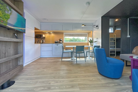 Interno di una tiny house moderna con cucina attrezzata, sala da pranzo, poltrone e letti a castello.