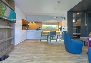 Moderne tiny house med fuldt udstyret køkken, spiseplads, opholdsområde og køjesenge i baggrunden.