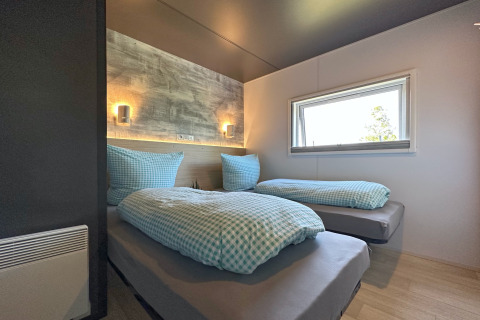 Moderne slaapkamer in een tiny house met twee eenpersoonsbedden, blauw geruit beddengoed en raam.