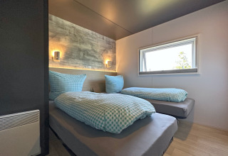Camera moderna in una tiny house con due letti singoli, biancheria a quadretti blu e finestra luminosa.