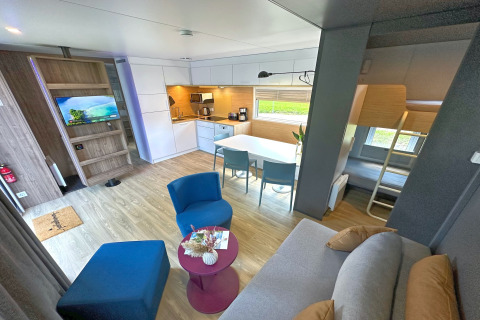 Interior de una tiny house moderna con cocina abierta, mesa de comedor, sala y literas en la esquina.