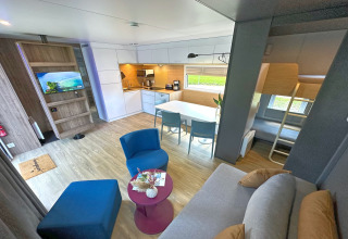 Modern tiny house-interieur met open keuken, eettafel, zithoek en stapelbedden in de hoek.