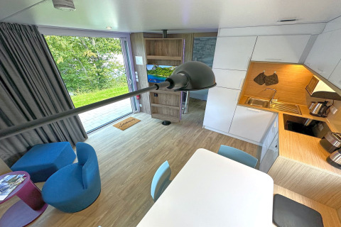 Interno moderno di una tiny house con cucina compatta, zona pranzo e vista panoramica sulla natura.