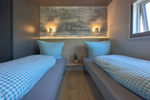 Moderne soveværelse i et tiny house med to enkeltsenge, lyseblåt sengetøj og naturligt lys fra vinduet.