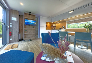 Moderne og lys stue i et tiny house med åbent køkken, spiseplads, blå stole og udsigt til naturen.