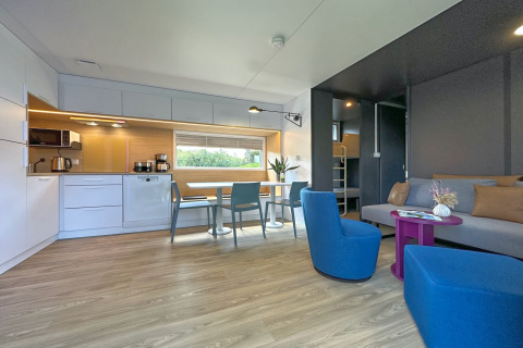 Intérieur de tiny house moderne avec cuisine, table à manger, chaises bleues et canapé confortable.