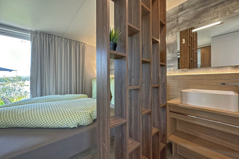 Moderne tiny house med soveplads og badeværelse adskilt af træhylde, naturligt lys og minimalistisk design.