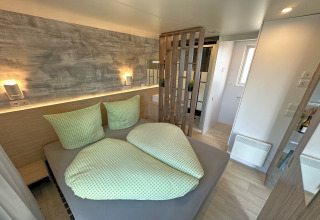 Moderne soveværelse i et tiny house med grønt tekstil, trægulv og adskillelse til badeværelse.