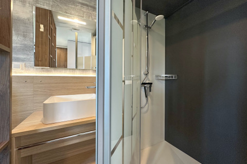 Moderne compacte badkamer in een tiny house met glazen douchecabine, houten wastafelmeubel en waskom.