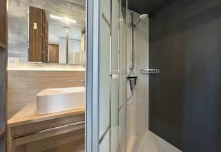 Moderne og kompakt badeværelse med glasbrusekabine, træbordplade og stor vask i et tiny house.