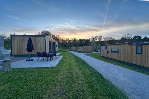 Moderne tiny houses van hout met terras en tuinmeubelen bij zonsondergang in een rustig vakantiepark.