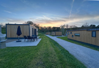 Modern tiny houses with wooden exteriors, patio furniture, and garden at sunset in a peaceful resort.