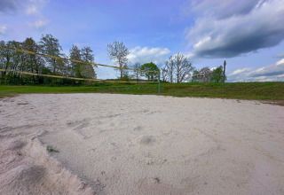 Buiten volleybalveld met wit zand en groene omgeving bij een tiny house onder een blauwe lucht.