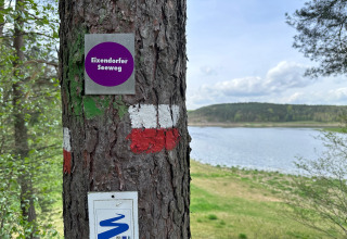 Boom met Eixendorfer Seeweg bordje aan een meer, met groene natuur en heuvels op de achtergrond.
