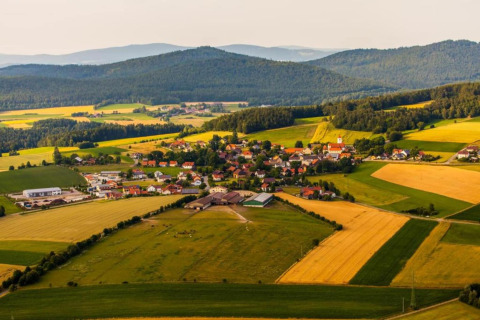 Luftaufnahme eines kleinen Dorfs mit Feldern und bewaldeten Hügeln, aufgenommen bei einem Tiny House.