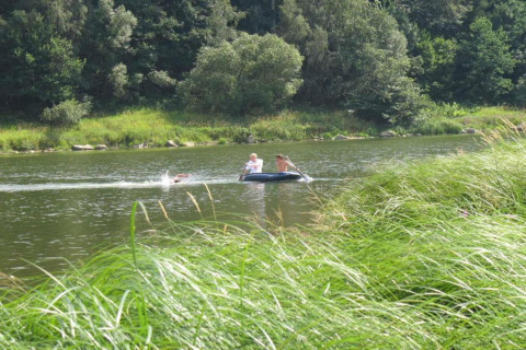 Two people paddle a small inflatable boat on a calm lake near Holiday village SEEBLICK as one person swims.