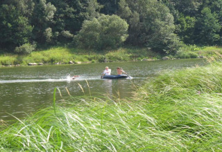 Two people paddle a small inflatable boat on a calm lake near Holiday village SEEBLICK as one person swims.