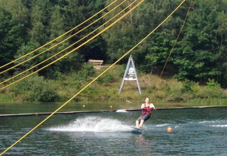 Eine Person fährt Wasserski an einer Seilbahn auf dem See bei Holiday village SEEBLICK - Tiny Chalet am Eixendorfer See.
