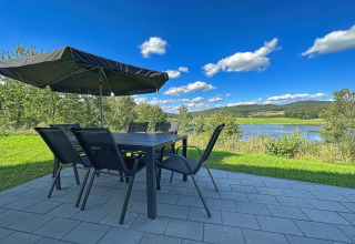 Terrasse mit Tisch, Stühlen und Sonnenschirm, Seeblick auf den Eixendorfer See und grüne Hügel, Deutschland.