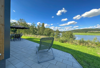 Udendørs terrasse med stole og bord, udsigt over søen Eixendorfer See og grønne bakker i Tyskland.