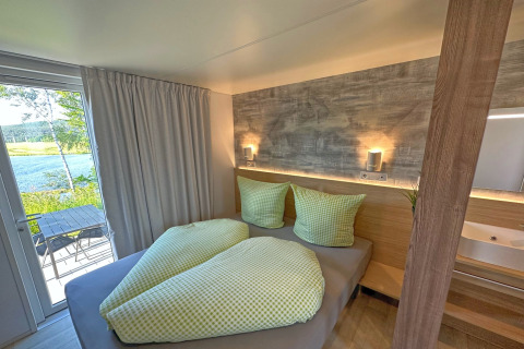 Schlafzimmer im Tiny Chalet am Eixendorfer See mit Blick auf Terrasse und See, grüne Bettwäsche.