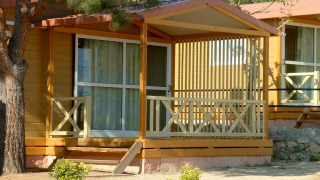 Camping Rocagrossa Bungalow für 4 Personen mit Veranda, Holzwänden und umgeben von Bäumen und Sträuchern.