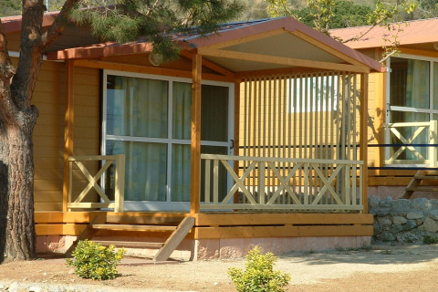 Udsigt til Camping Rocagrossa Bungalow til 4 personer med terrasse og træpaneler, omgivet af planter.