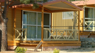 Camping Rocagrossa Bungalow für 4 Personen mit Veranda, Holzwänden und umgeben von Bäumen und Sträuchern.