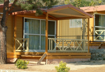Camping Rocagrossa Bungalow for 4 people featuring a porch, wooden railings, and surrounded by greenery.