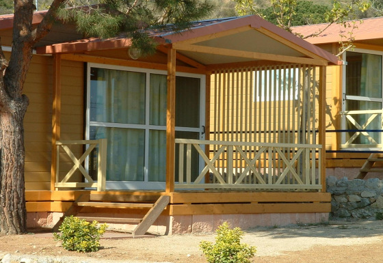 Udsigt til Camping Rocagrossa Bungalow til 4 personer med terrasse og træpaneler, omgivet af planter.