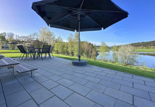 Terraza con sombrilla y muebles de jardín con vistas al lago en SEEBLICK Tiny Chalet en Alemania.