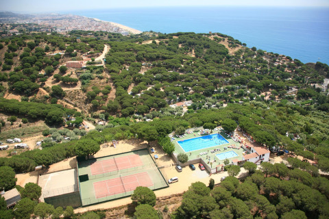 Vista aerea di un glamping con piscine, campi da tennis, alberi rigogliosi e vista mare vicino a una città.