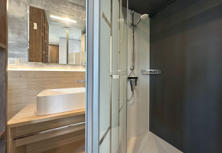 Salle de bain moderne dans un tiny house, vasque rectangulaire, bois, miroir et douche noire.