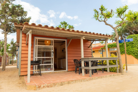 Camping del Mar BUNGALOW MEDITERRANI met een terras, tuinstoelen en bomen in een rustige natuurlijke omgeving.