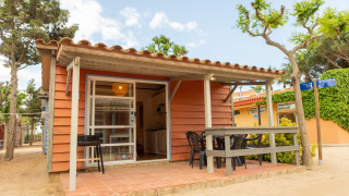 Camping del Mar BUNGALOW MEDITERRANI met een terras, tuinstoelen en bomen in een rustige natuurlijke omgeving.