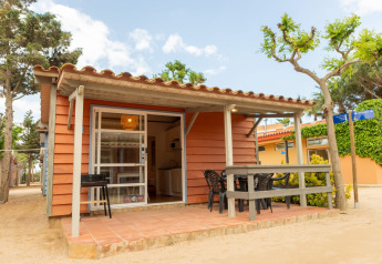 Camping del Mar BUNGALOW MEDITERRANI with a small porch, outdoor seating, and trees in a serene atmosphere.