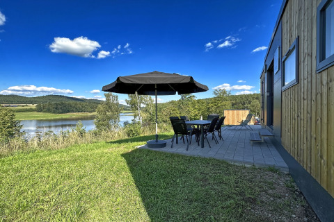 Blick von der Terrasse des Holiday village SEEBLICK - Tiny Chalet am Eixendorfer See mit Tisch, Stühlen und Sonnenschirm.