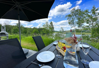 Outdoor dining table with plates, fruit, flowers, and lake view at Holiday village SEEBLICK Tiny Chalet Eixendorfer See.