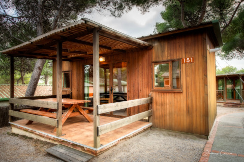 Bungalow de madera en Vilanova Park, terraza cubierta y mesa de picnic, rodeado de árboles, número 151.