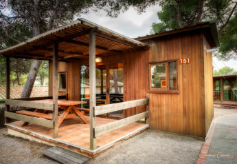 Bungalow de madera en Vilanova Park, terraza cubierta y mesa de picnic, rodeado de árboles, número 151.