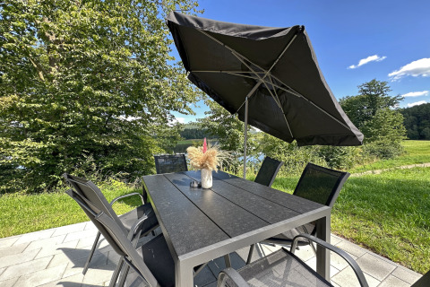 Outdoor table and chairs with a black umbrella at Holiday village SEEBLICK - Tiny Chalet am Eixendorfer See, Germany.