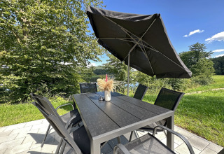 Outdoor table and chairs with a black umbrella at Holiday village SEEBLICK - Tiny Chalet am Eixendorfer See, Germany.