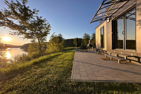 Modern tiny house met terras aan het Eixendorfer See in Duitsland, omgeven door natuur bij zonsondergang.