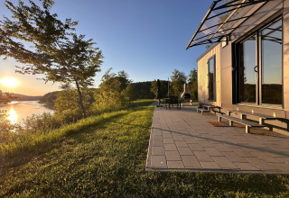 Modern tiny house met terras aan het Eixendorfer Meer, omgeven door groen en zonsondergang.
