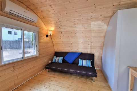 Interior view of Nomad Paraiso pod in Spain featuring wood walls, black sofa and blue cushions.